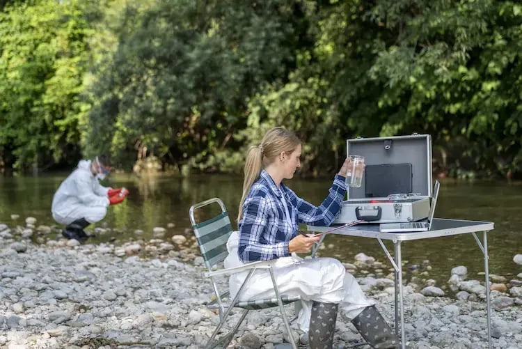 Scientist testing water quality by a river.