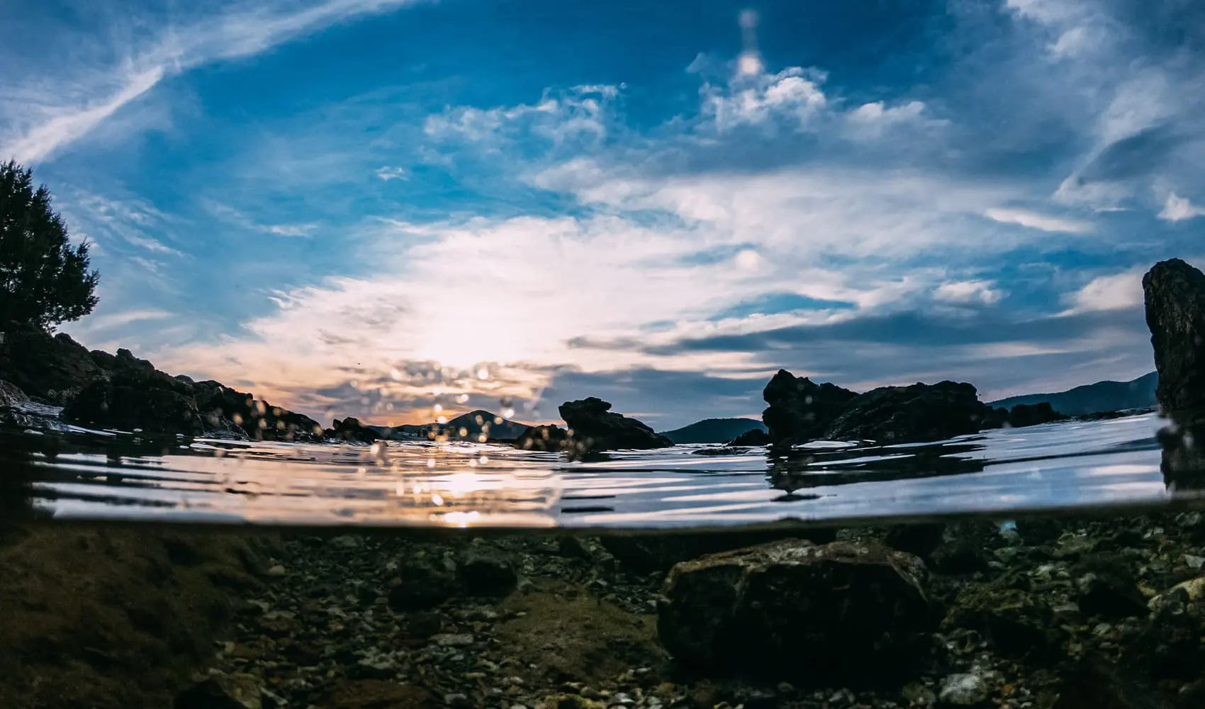 Split view of a rocky coastline and cloudy sunset from the water's surface.