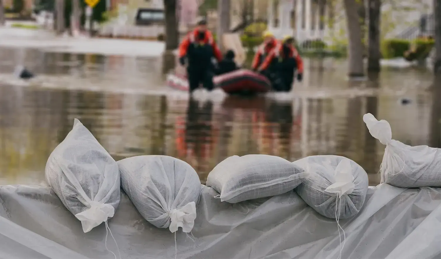 Rescue team in boat behind sandbag flood barrier.