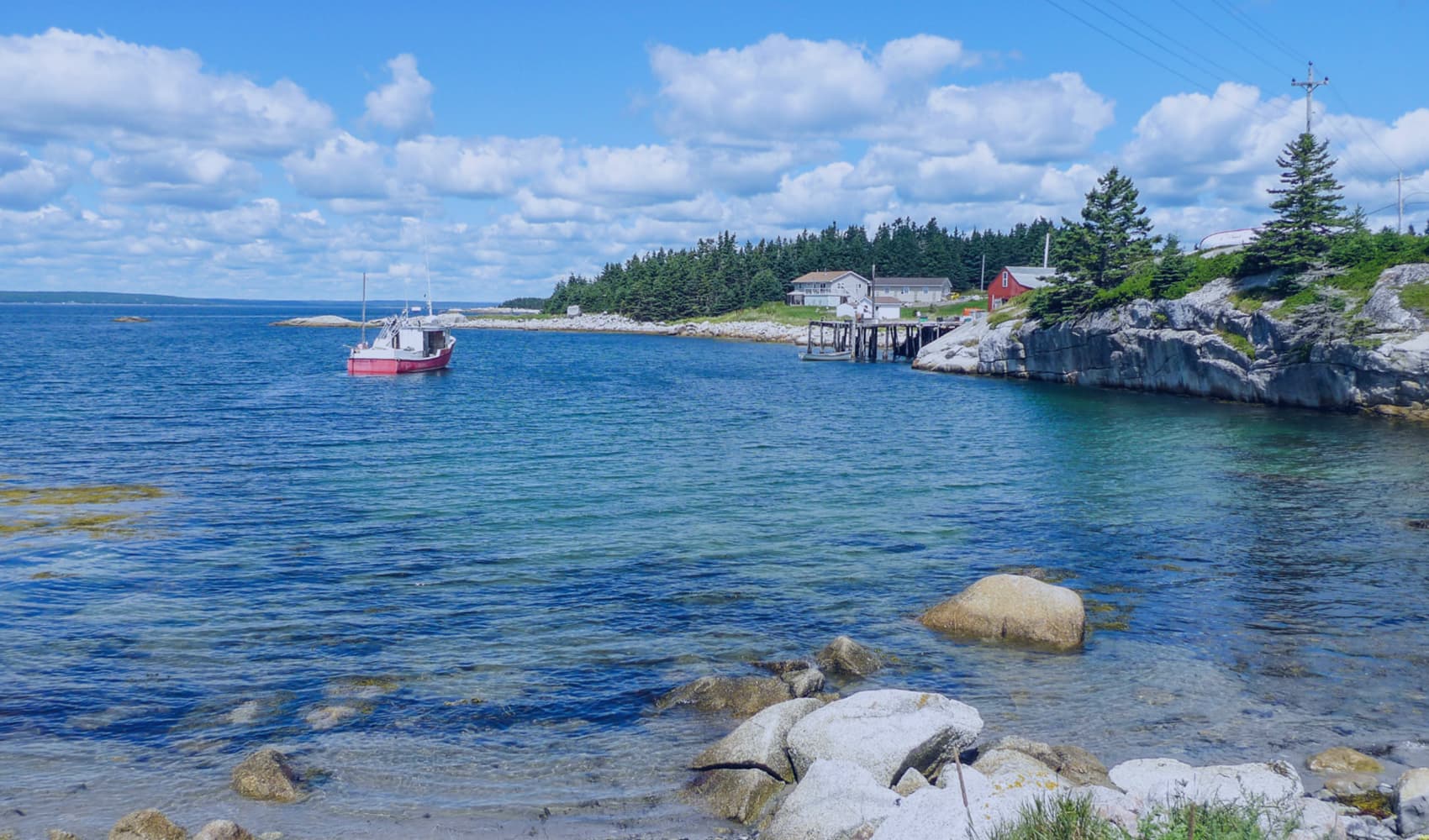 Coastal scene in Atlantic Canada with a red boat, rocky shores, and lush greenery.