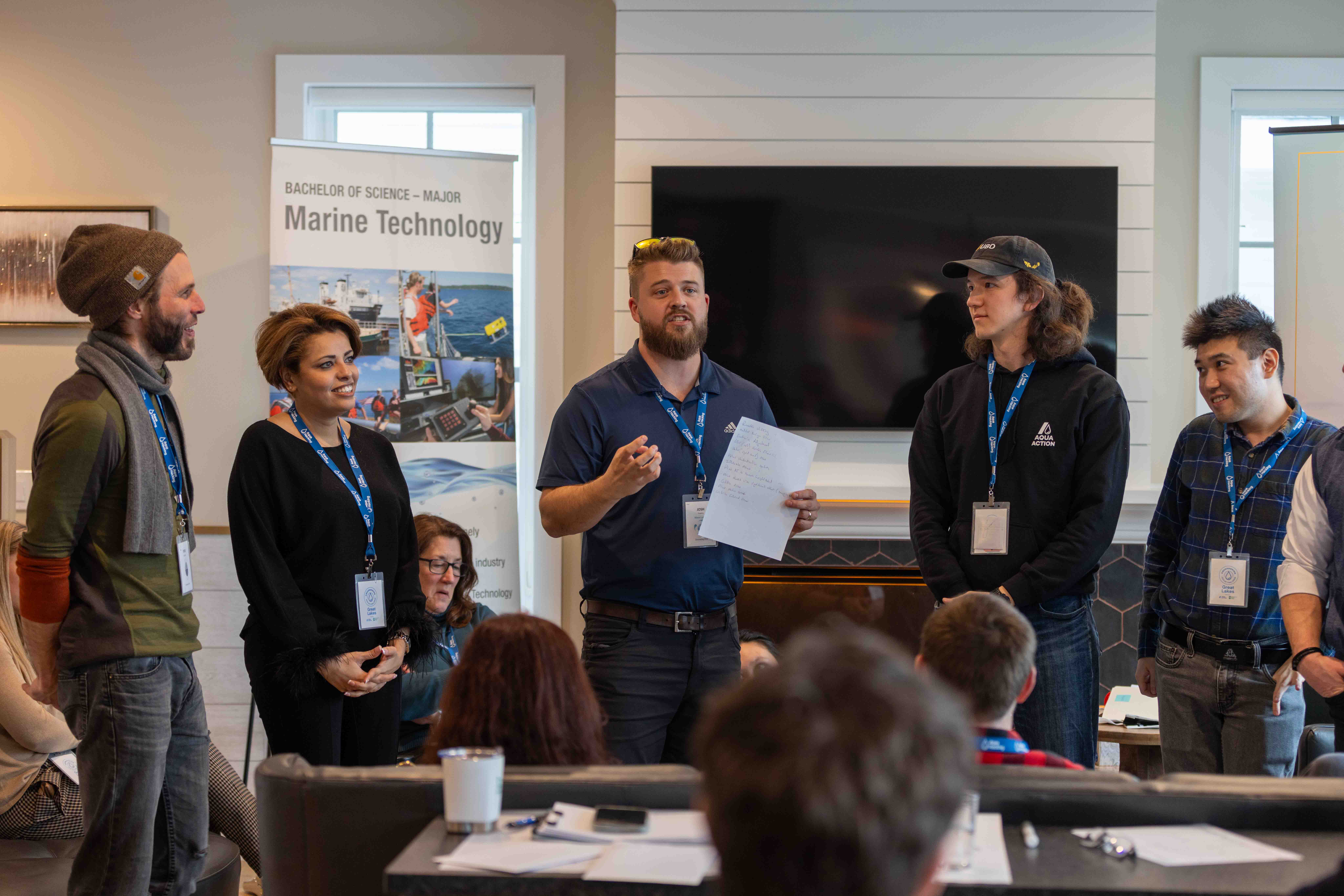 A group of participants standing and presenting during an AquaAction workshop, with a “Marine Technology” banner in the background, representing collaboration and innovation in environmental solutions.