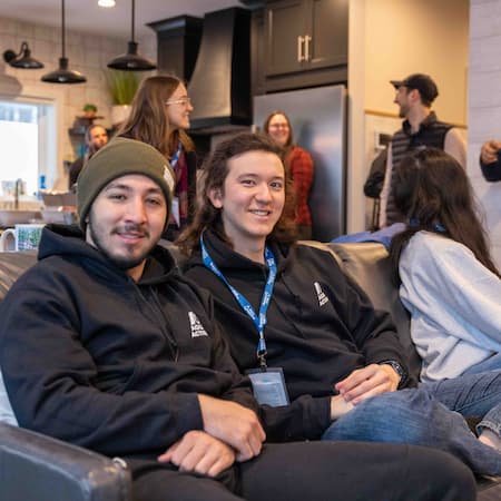 A group of young people from our AquaHacking program in a cozy indoor setting, with two smiling participants wearing AquaHacking hoodies, representing teamwork, innovation, and environmental problem-solving.