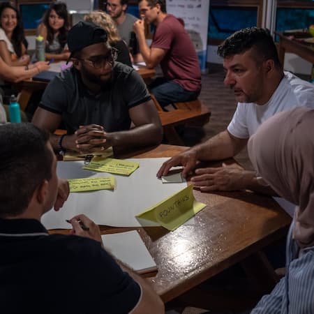 A diverse group of people engaged in a brainstorming session around a wooden table, discussing innovative solutions for water-related challenges.