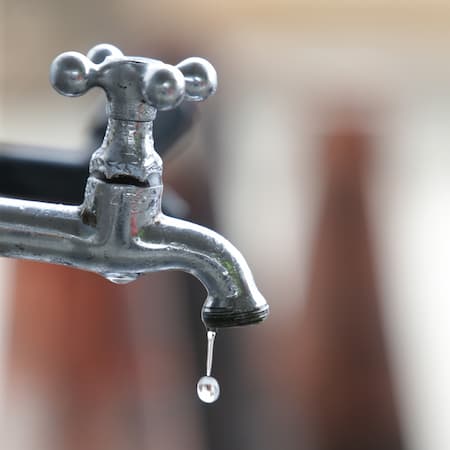 A close-up of an old metal faucet with a single droplet of water falling, emphasizing the importance of water conservation and leakage prevention.