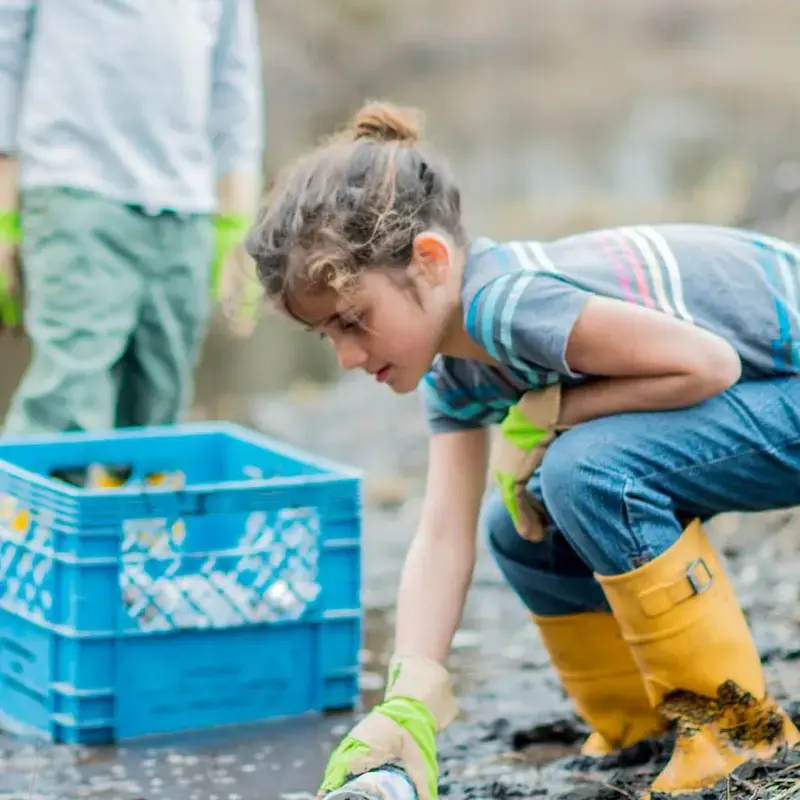 A child volunteers in river cleanup, picking up litter.